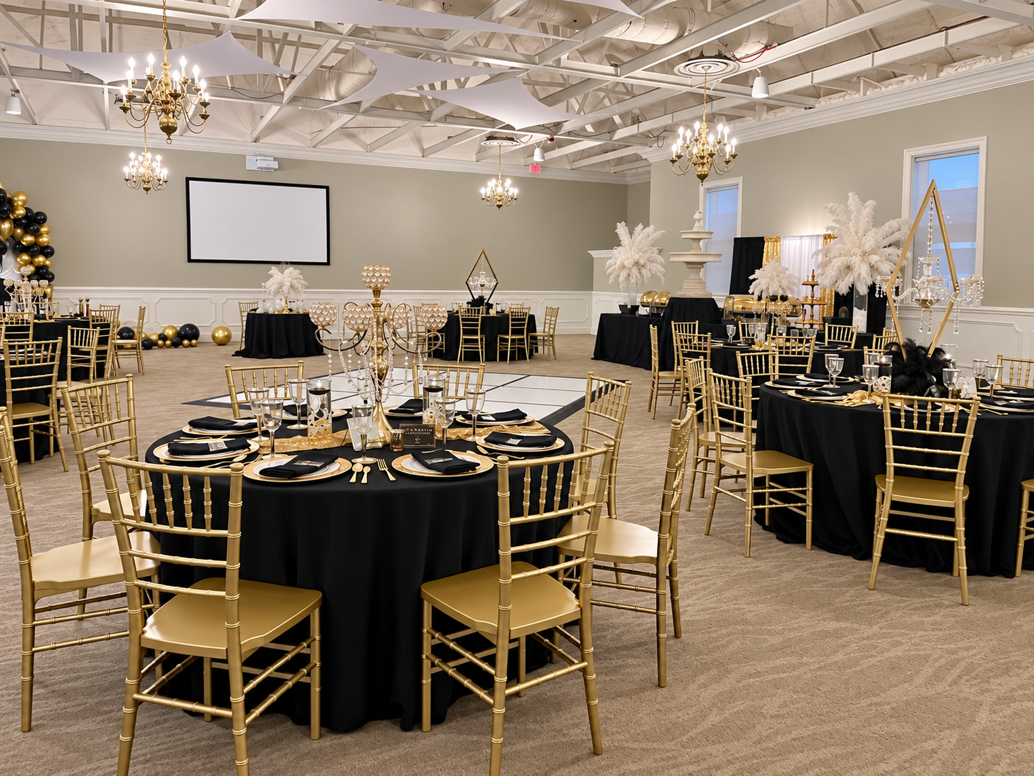 Black and gold banquet room with coordinated tables, gold chairs, chandeliers, and white florals.